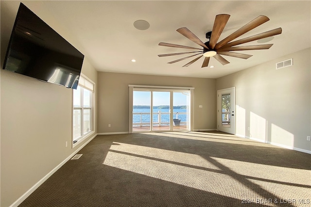 unfurnished living room with ceiling fan, a water view, and dark colored carpet