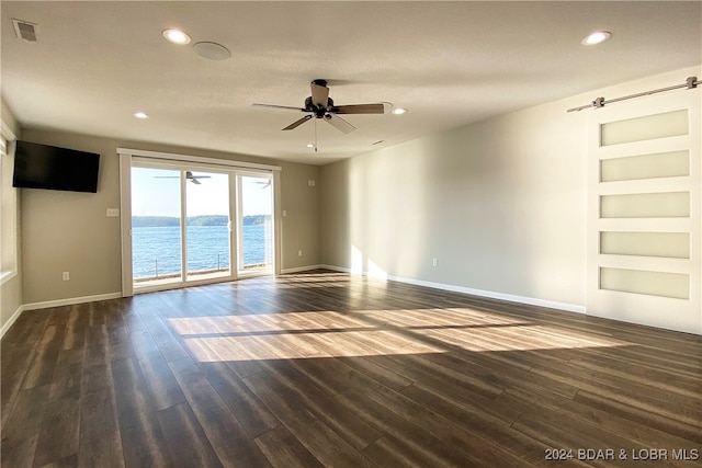 unfurnished room featuring a water view, dark hardwood / wood-style floors, ceiling fan, built in features, and a textured ceiling