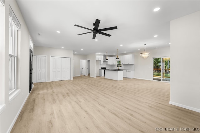 unfurnished living room with ceiling fan with notable chandelier and light hardwood / wood-style flooring