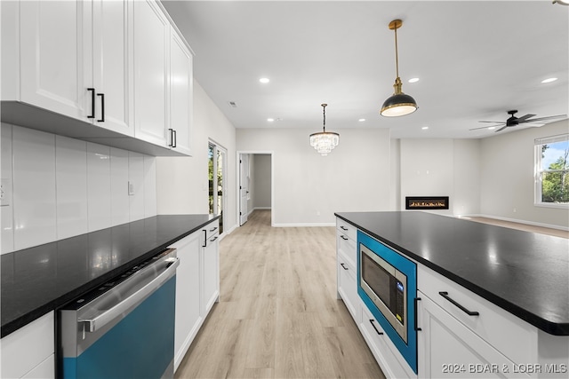 kitchen with light hardwood / wood-style floors, pendant lighting, a large fireplace, white cabinets, and appliances with stainless steel finishes