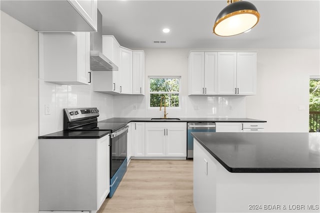 kitchen with sink, light hardwood / wood-style flooring, wall chimney range hood, white cabinetry, and appliances with stainless steel finishes