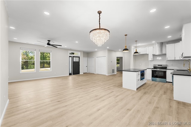 kitchen featuring white cabinets, wall chimney exhaust hood, light hardwood / wood-style floors, hanging light fixtures, and appliances with stainless steel finishes