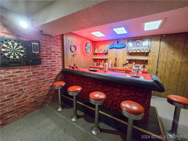 bar with carpet floors, a textured ceiling, wood walls, and brick wall