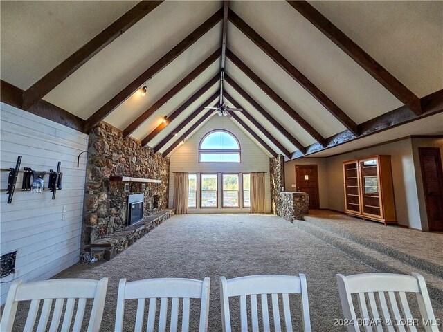 unfurnished living room with carpet floors, a stone fireplace, wooden walls, and high vaulted ceiling