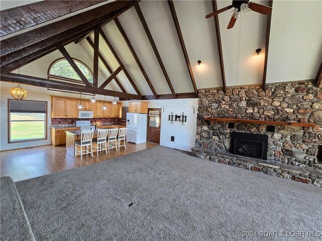 unfurnished living room with a stone fireplace, beam ceiling, dark hardwood / wood-style flooring, and high vaulted ceiling