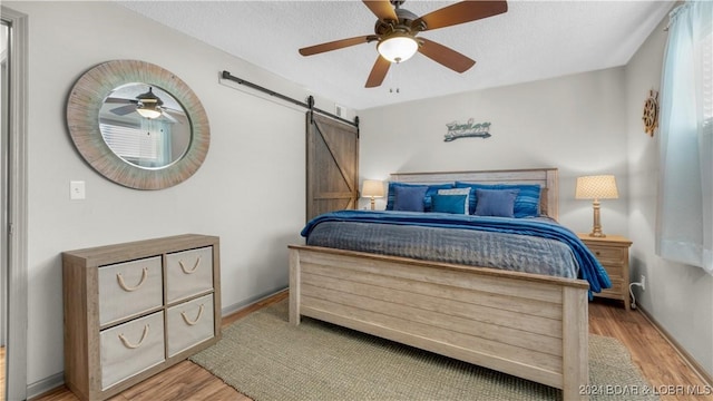 bedroom with a barn door, ceiling fan, a textured ceiling, and light wood-type flooring