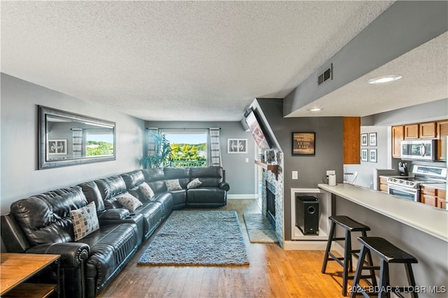 living room featuring a stone fireplace, light wood-type flooring, and a textured ceiling