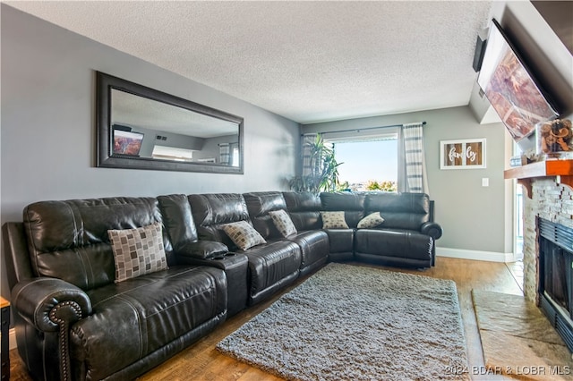 living room with wood-type flooring, a stone fireplace, vaulted ceiling, and a textured ceiling