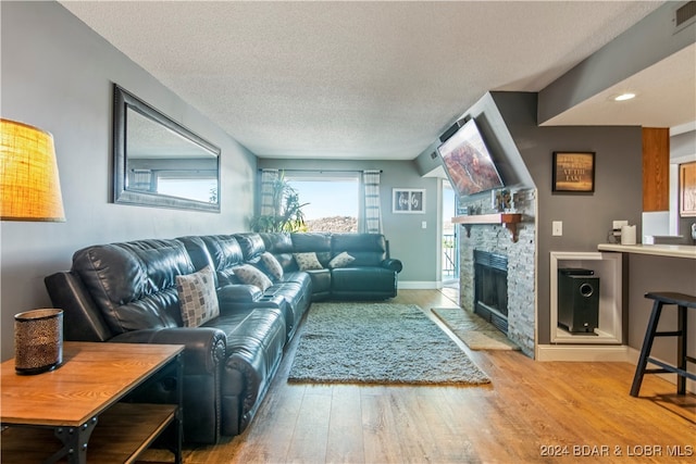 living room featuring a stone fireplace, a textured ceiling, and light wood-type flooring