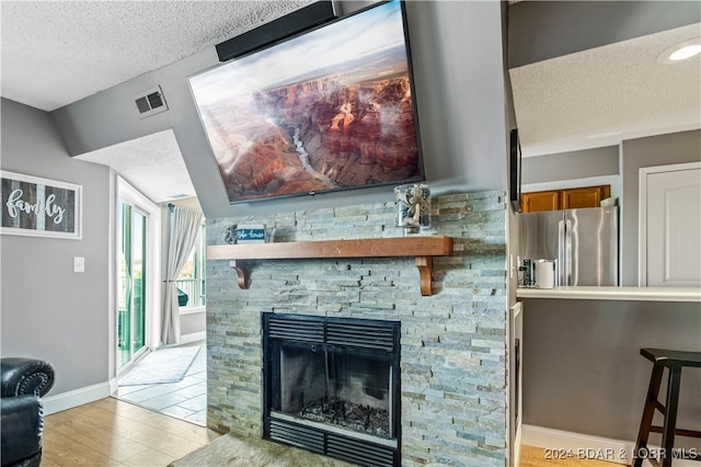 living room featuring lofted ceiling, a fireplace, light hardwood / wood-style flooring, and a textured ceiling