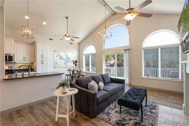 living room featuring ceiling fan with notable chandelier, light hardwood / wood-style floors, high vaulted ceiling, and sink