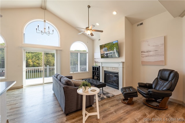 living room featuring light hardwood / wood-style floors, ceiling fan with notable chandelier, beam ceiling, a fireplace, and high vaulted ceiling