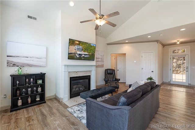 living room with high vaulted ceiling, ceiling fan, a tile fireplace, and light hardwood / wood-style floors