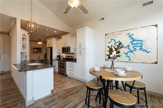 kitchen featuring dark hardwood / wood-style flooring, decorative light fixtures, kitchen peninsula, white cabinets, and appliances with stainless steel finishes