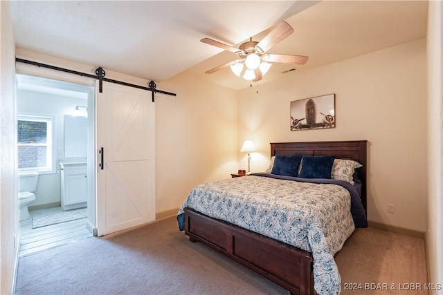 carpeted bedroom featuring a barn door, connected bathroom, and ceiling fan