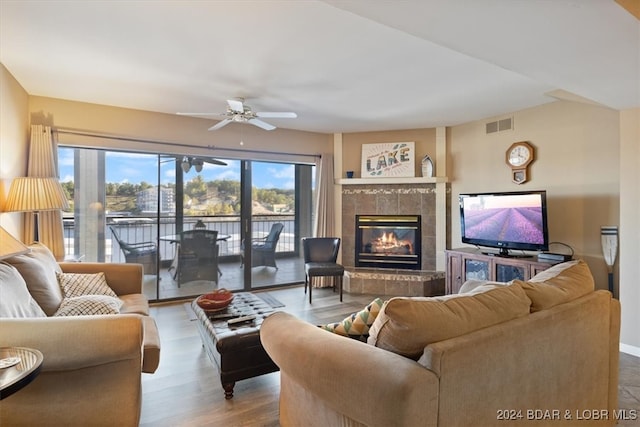 living room with ceiling fan, light wood-type flooring, and a tile fireplace