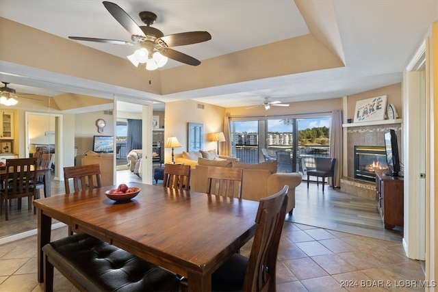 dining space featuring ceiling fan, a fireplace, tile patterned flooring, and a tray ceiling