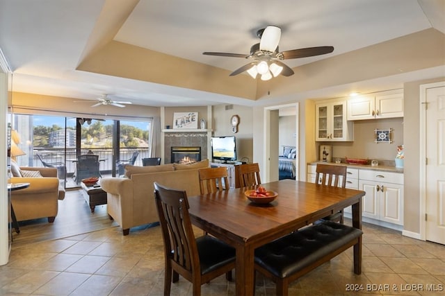 dining area with ceiling fan, a raised ceiling, light hardwood / wood-style floors, and a tile fireplace