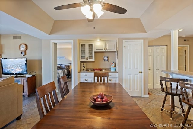 tiled dining space featuring a raised ceiling, decorative columns, and ceiling fan