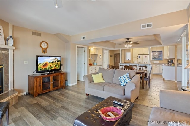 living room featuring a fireplace, a raised ceiling, hardwood / wood-style floors, and ceiling fan