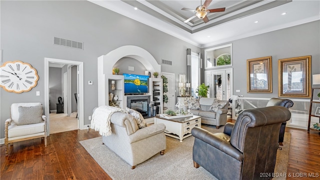 living room featuring wood-type flooring, a tray ceiling, ceiling fan, a high ceiling, and ornamental molding