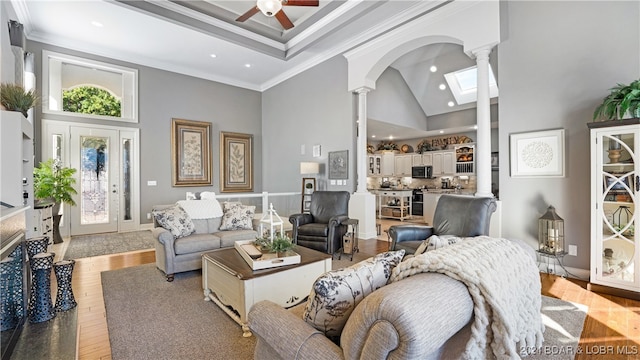 living room with a wealth of natural light, ornamental molding, light wood-type flooring, and high vaulted ceiling