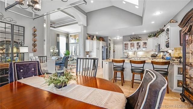 tiled dining room with a chandelier, high vaulted ceiling, sink, and ornate columns