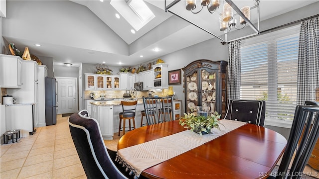 tiled dining room featuring high vaulted ceiling, a skylight, and a chandelier