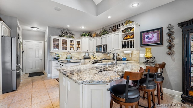 kitchen featuring kitchen peninsula, stainless steel appliances, backsplash, light stone countertops, and white cabinetry