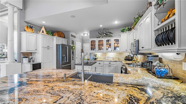 kitchen featuring decorative columns, light stone countertops, white cabinets, appliances with stainless steel finishes, and tasteful backsplash