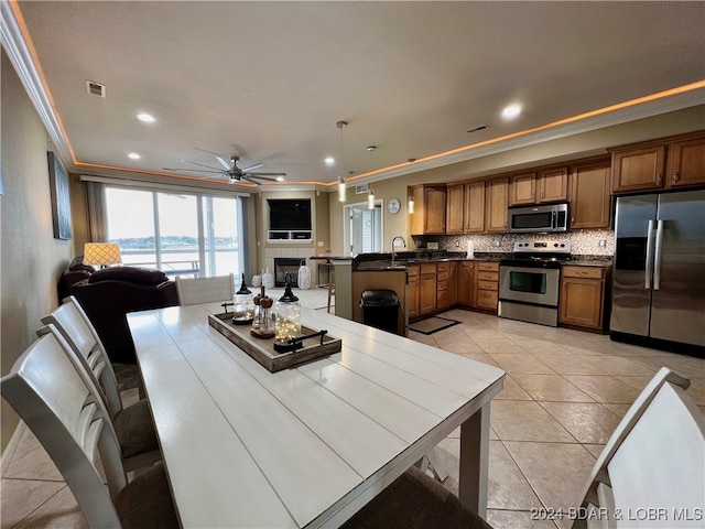 kitchen with ornamental molding, appliances with stainless steel finishes, kitchen peninsula, and hanging light fixtures