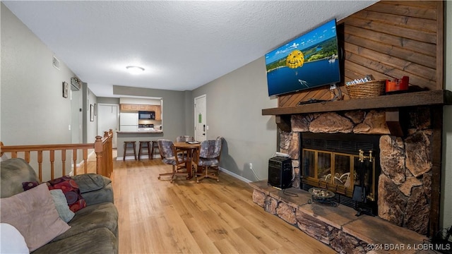 living room featuring light wood-type flooring, a stone fireplace, and a textured ceiling