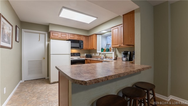 kitchen featuring a sink, electric range oven, freestanding refrigerator, a peninsula, and black microwave