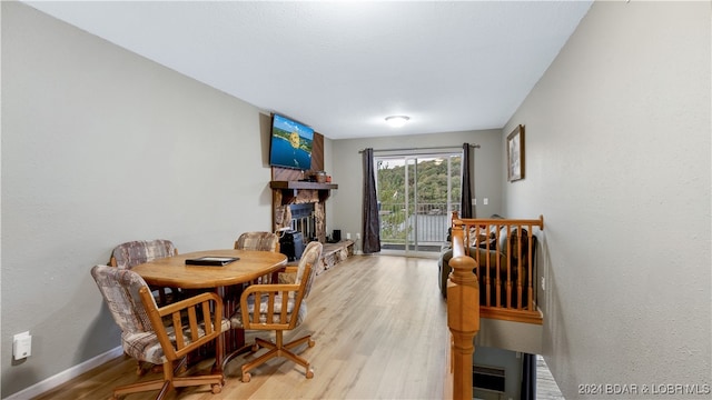 dining room featuring light wood-type flooring, baseboards, and a stone fireplace