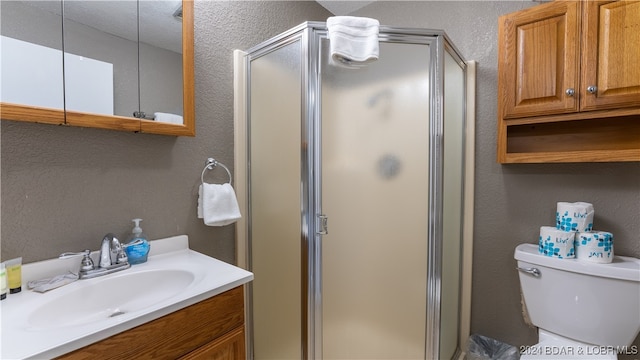 bathroom featuring vanity, toilet, a textured wall, and a stall shower