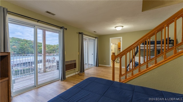 bedroom with access to exterior, visible vents, a textured ceiling, and wood finished floors