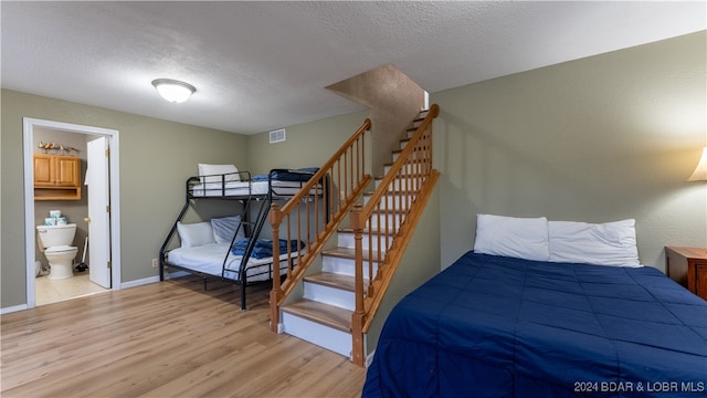 bedroom with visible vents, light wood-style flooring, a textured ceiling, and baseboards