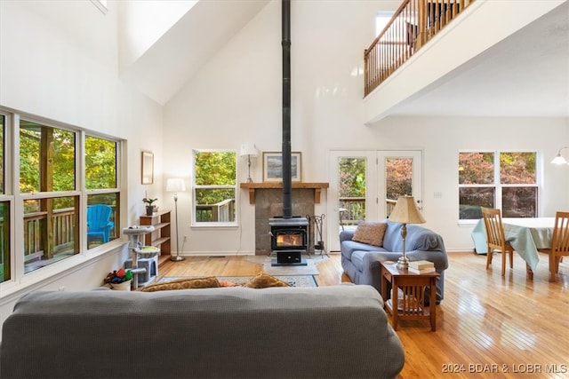 living room featuring a towering ceiling, a wealth of natural light, light wood-type flooring, and a wood stove