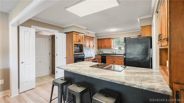 kitchen with tasteful backsplash, black appliances, light wood-type flooring, a kitchen bar, and ornamental molding