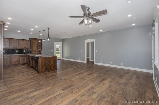 kitchen with decorative backsplash, light stone counters, an island with sink, dark hardwood / wood-style floors, and decorative light fixtures