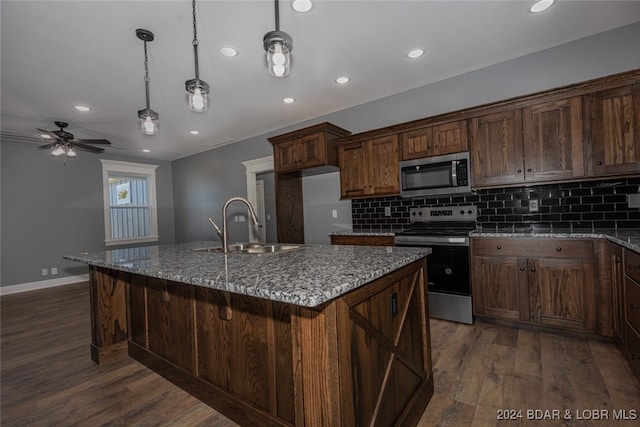 kitchen featuring a kitchen island with sink, hanging light fixtures, stainless steel appliances, sink, and dark hardwood / wood-style flooring