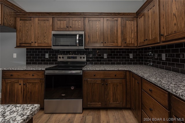 kitchen with light stone countertops, backsplash, dark brown cabinets, light hardwood / wood-style floors, and stainless steel appliances