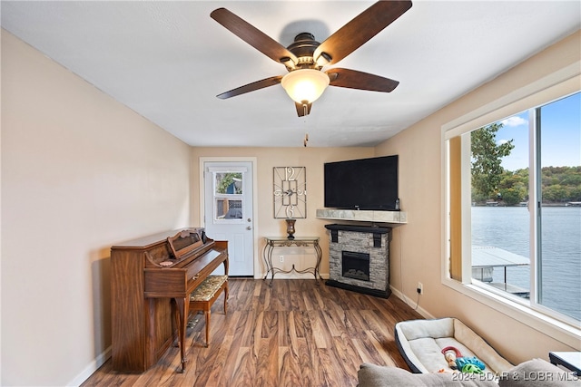 living room featuring ceiling fan, a stone fireplace, and dark hardwood / wood-style flooring