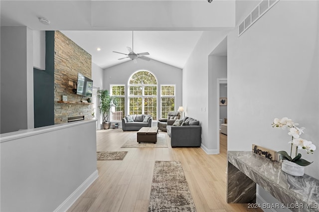 living room featuring ceiling fan, lofted ceiling, light wood-type flooring, and a fireplace