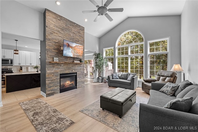 living room featuring light hardwood / wood-style floors, a stone fireplace, high vaulted ceiling, and ceiling fan