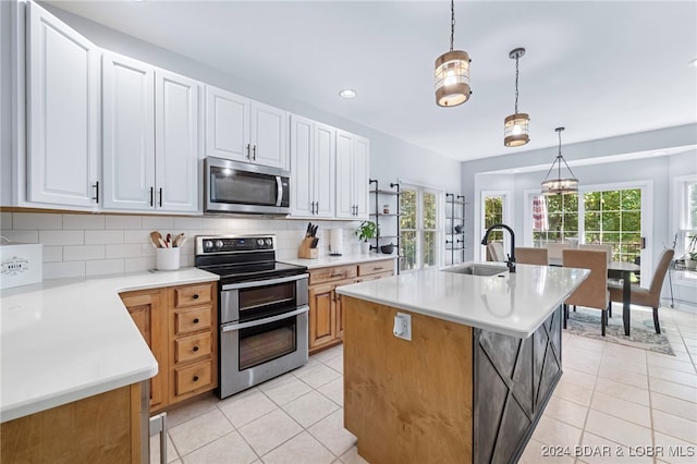 kitchen featuring an island with sink, hanging light fixtures, sink, white cabinetry, and appliances with stainless steel finishes