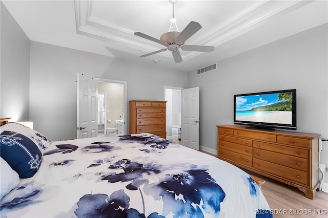 bedroom with ceiling fan, a raised ceiling, light hardwood / wood-style flooring, crown molding, and ensuite bath