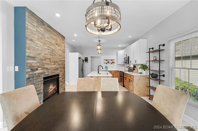 interior space with white cabinets, an island with sink, sink, a stone fireplace, and stainless steel appliances