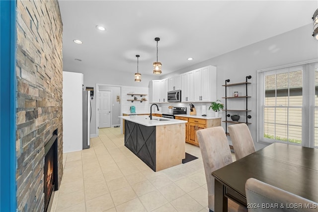 kitchen featuring light tile patterned floors, white cabinetry, a kitchen island with sink, pendant lighting, and stainless steel appliances