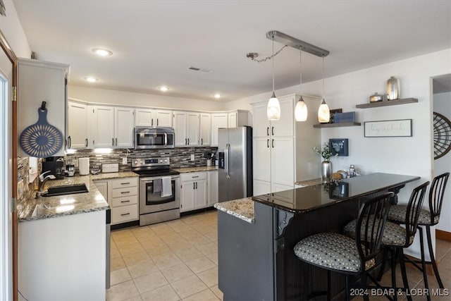 kitchen featuring hanging light fixtures, stainless steel appliances, kitchen peninsula, sink, and white cabinetry